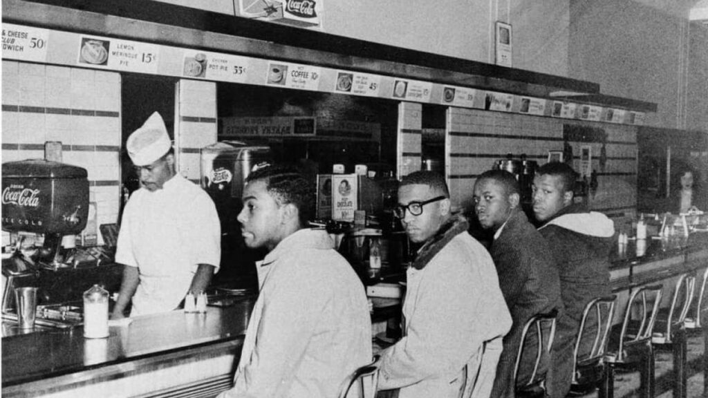 Black and white photo of four students conducting a non-violent sit-in at the F.W. Woolworth Department Store lunch counter in Greensboro, North Carolina.